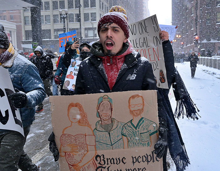 Protester in snowy street holding sign during heated debate on ICE immigration policies and SNL controversy.