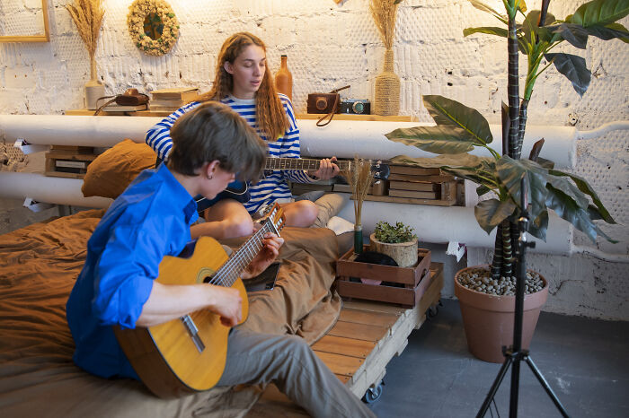 Two people playing guitars in a cozy room, sharing real-life cheat codes to improve their skills together.