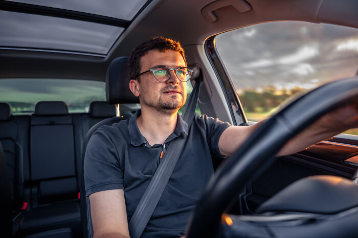 Man wearing glasses driving a car during sunset, focused and using a real-life cheat code for easier travel.