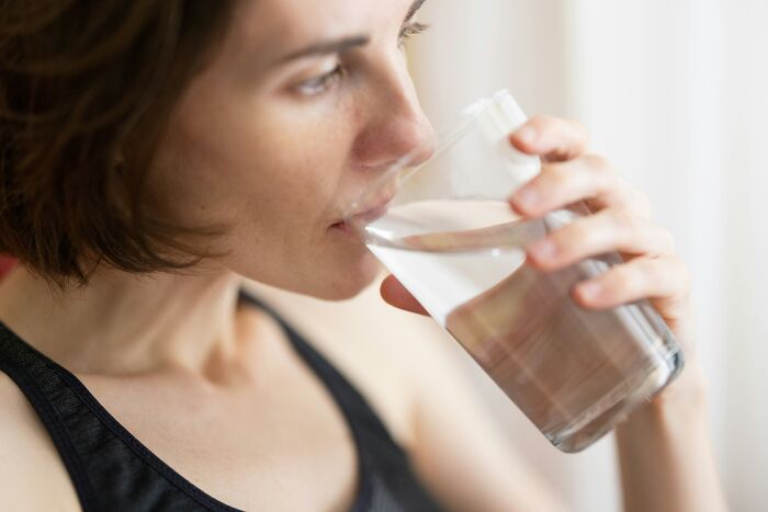 Woman drinking a glass of water as a real-life cheat code for staying healthy and hydrated every day.