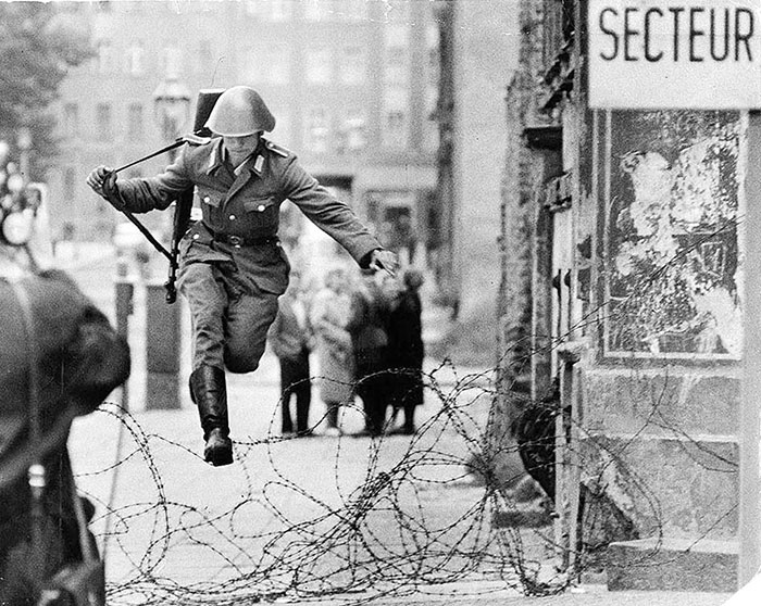 Soldier in historical war uniform jumping over barbed wire in a city street, powerful photo from countries that hit hard.