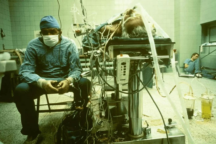 Surgeon resting beside patient on an operating table with complex medical equipment in a tense hospital scene reflecting impactful moments.