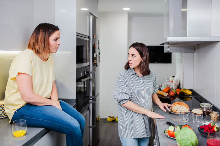 Two women in a kitchen having a serious conversation, sharing experiences about wildest ways people found out cheating.