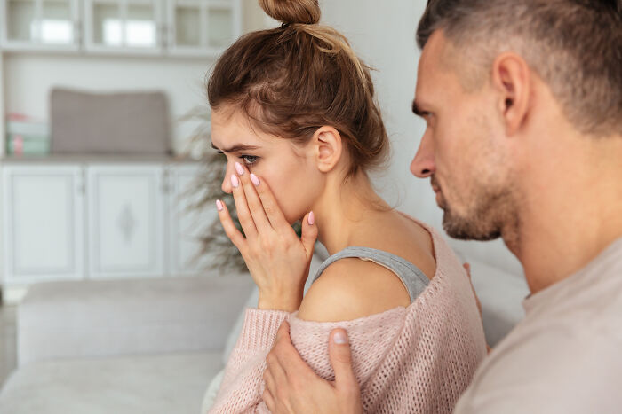 A distressed woman covers her face while a concerned man comforts her, depicting people share wildest ways found out cheating.