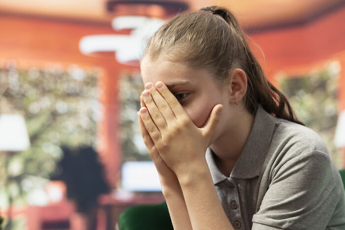 Teen girl covering her face with hands, appearing distressed and upset while thinking about worst person they've ever met stories.