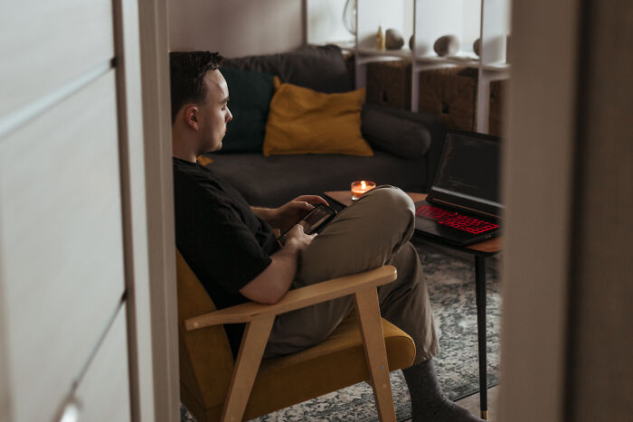 Man sitting in armchair with phone and laptop in cozy living room, reflecting on worst person stories shared by people.