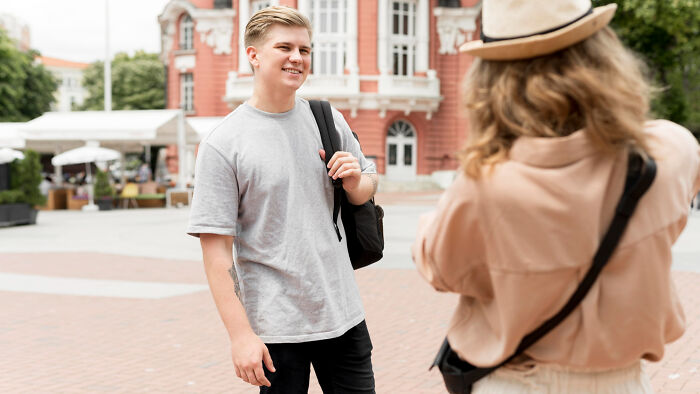 Young man smiling outdoors as friend photographs him, candid scene capturing incredible moments among travelers.