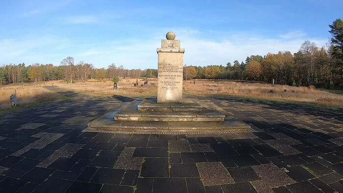 Stone monument on a paved plaza amid autumn fields and visitors, evoking weird or incredible moments people faced