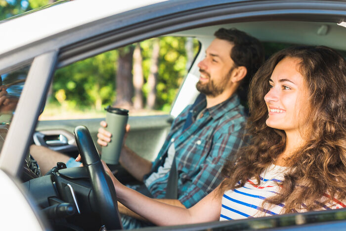 Moments People Faced: smiling young couple in a car, woman driving, man holding a travel mug, sunny day