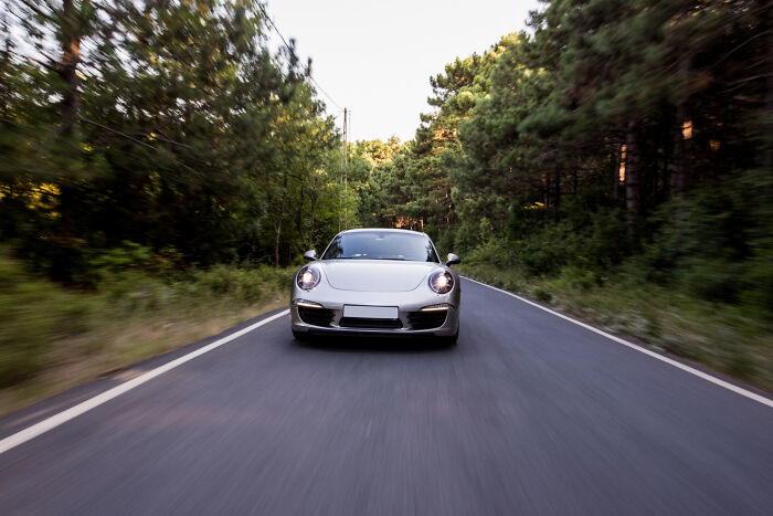 Silver sports car speeding down a tree-lined road with motion blur, incredible moments