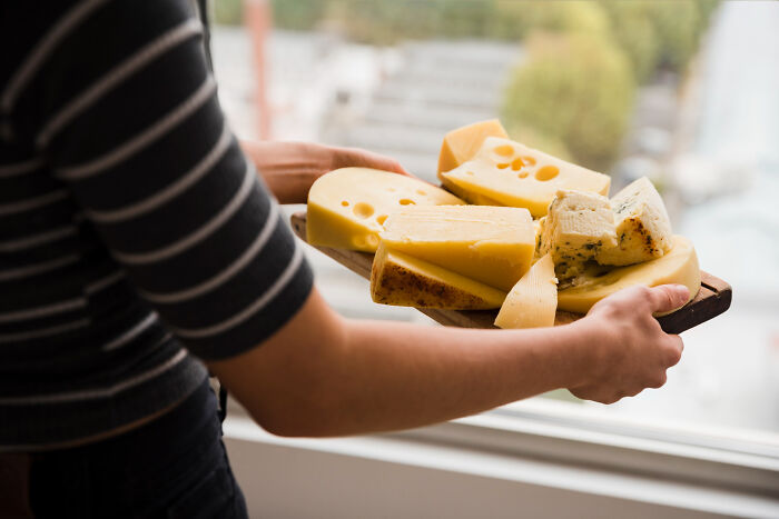 Person holding a wooden tray with various types of cheese, illustrating strange tales of folks who morphed.