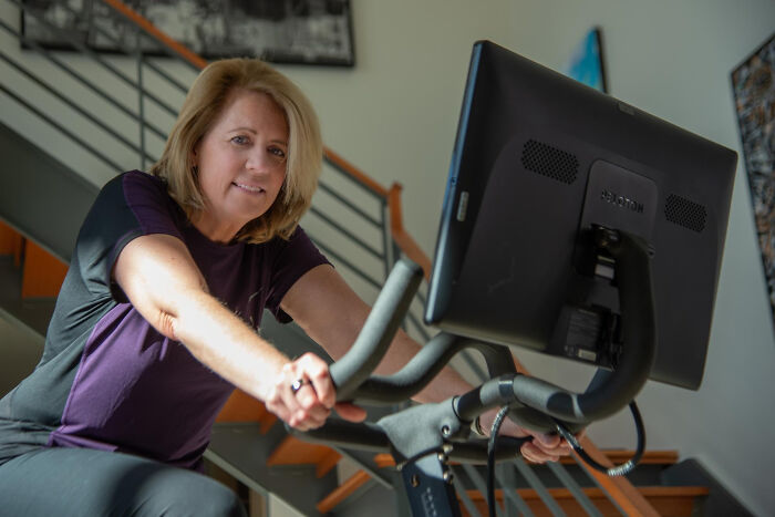 Middle-aged woman exercising on a stationary bike, illustrating strange tales of folks who morphed unexpectedly.