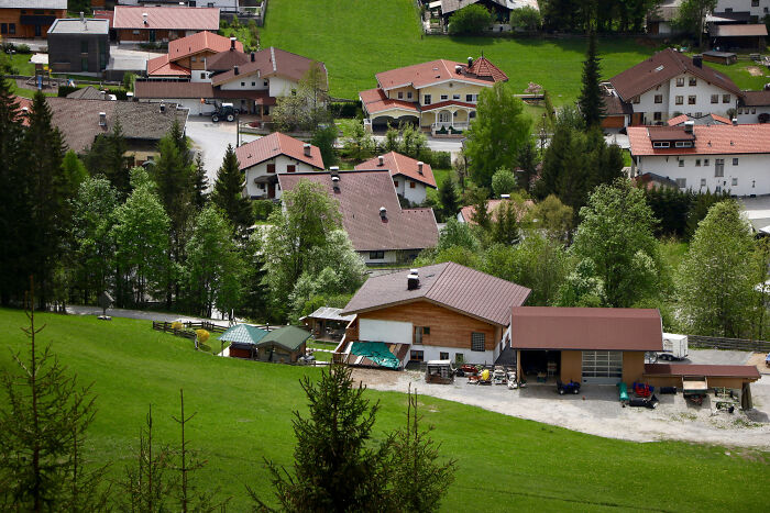 Aerial view of a rural village with houses surrounded by green fields and trees, illustrating strange tales of transformation.