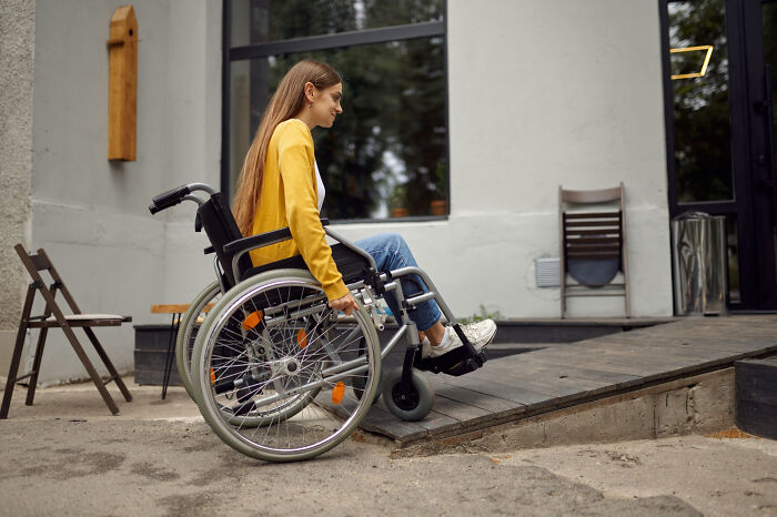 Young woman in a wheelchair maneuvering up a wooden ramp outside a building, illustrating strange tales of personal transformation.