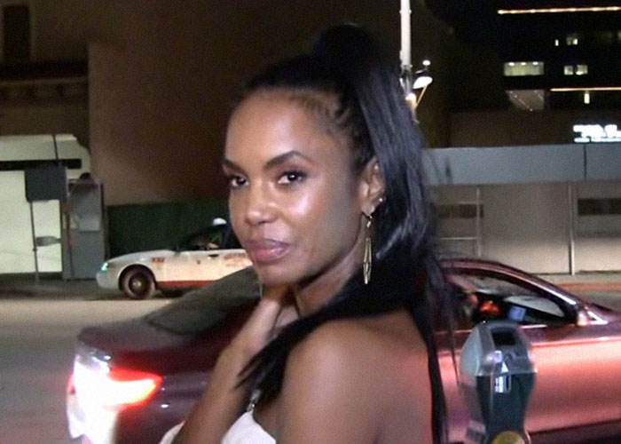 Woman with long dark hair in a ponytail standing near a parking meter, captured in a nighttime urban setting discussing celebrity passings.