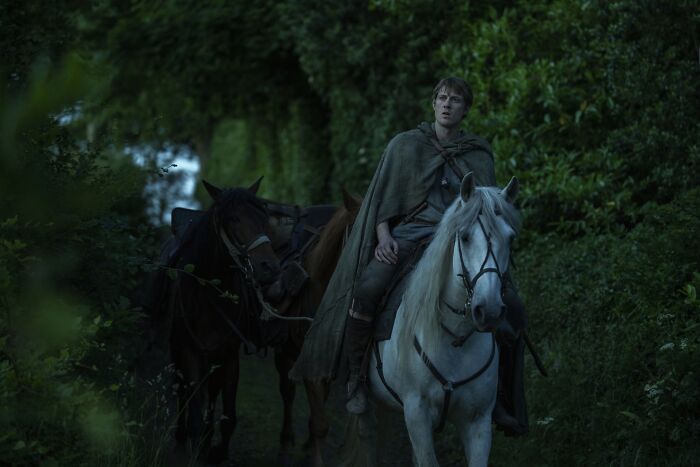 A young hedge knight riding a white horse through a dense forest in Knight of the Seven Kingdoms.