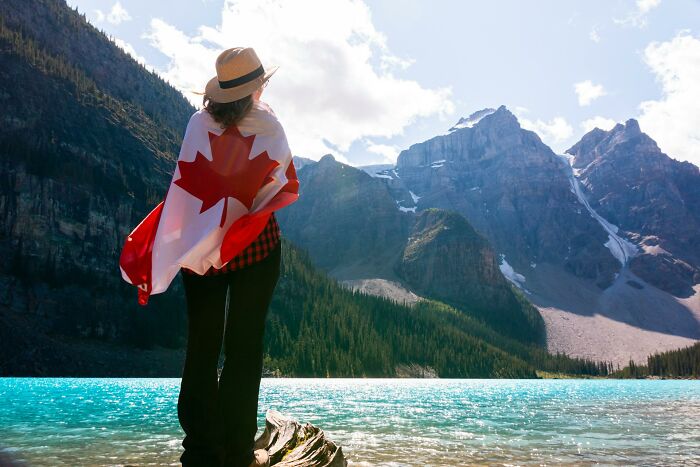 Person wrapped in Canadian flag overlooking turquoise lake and mountains, illustrating lesser-known facts about countries.