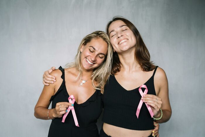 Two smiling women wearing black tops holding pink ribbons symbolizing progress and hope in America.