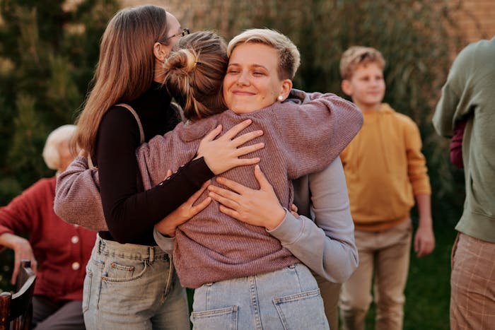 Woman sharing a warm group hug outdoors with multiple family members, highlighting unique parent relationships. Woman sharing a warm group hug outdoors with multiple family members, highlighting unique parent relationships.
