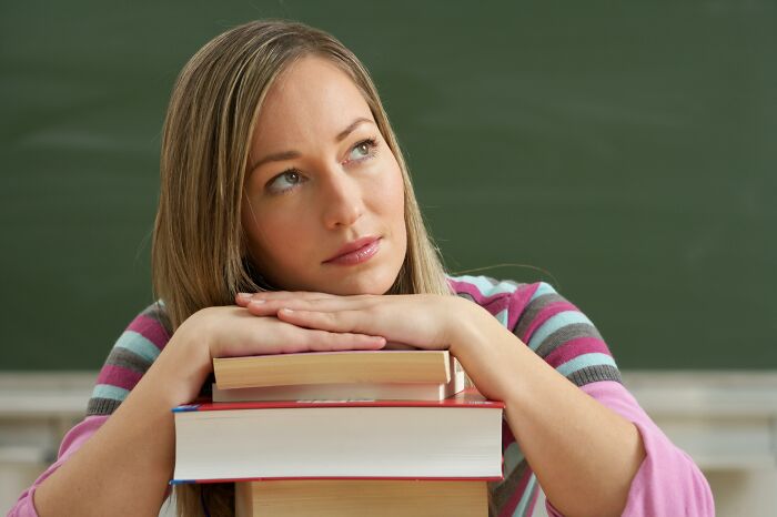 Young woman leaning on a stack of books, looking thoughtful, representing biggest family secrets and personal stories.