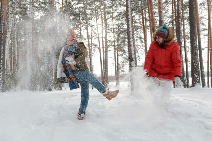 Two people playfully throwing snow in a snowy pine forest during winter, rained frogs