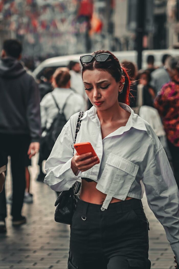 Young woman looking shocked while using her phone in a busy street, reflecting things that shocked people after prison.