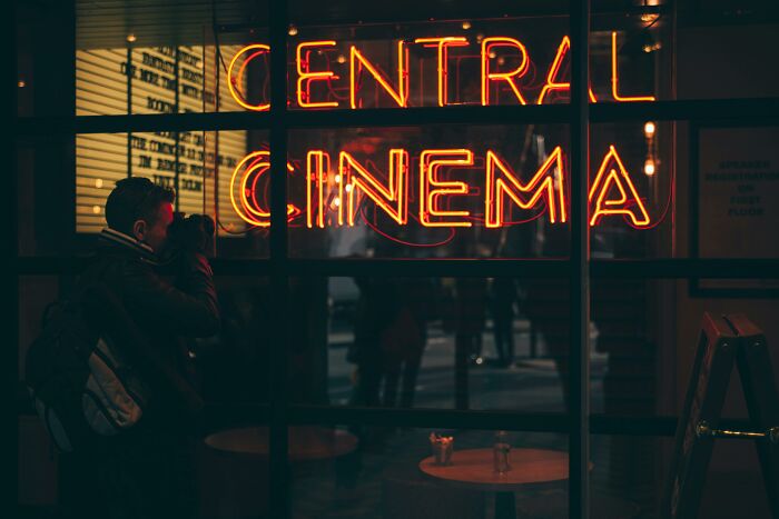 Person photographing neon Central Cinema sign through window at night, moody urban scene, movies quiz theme