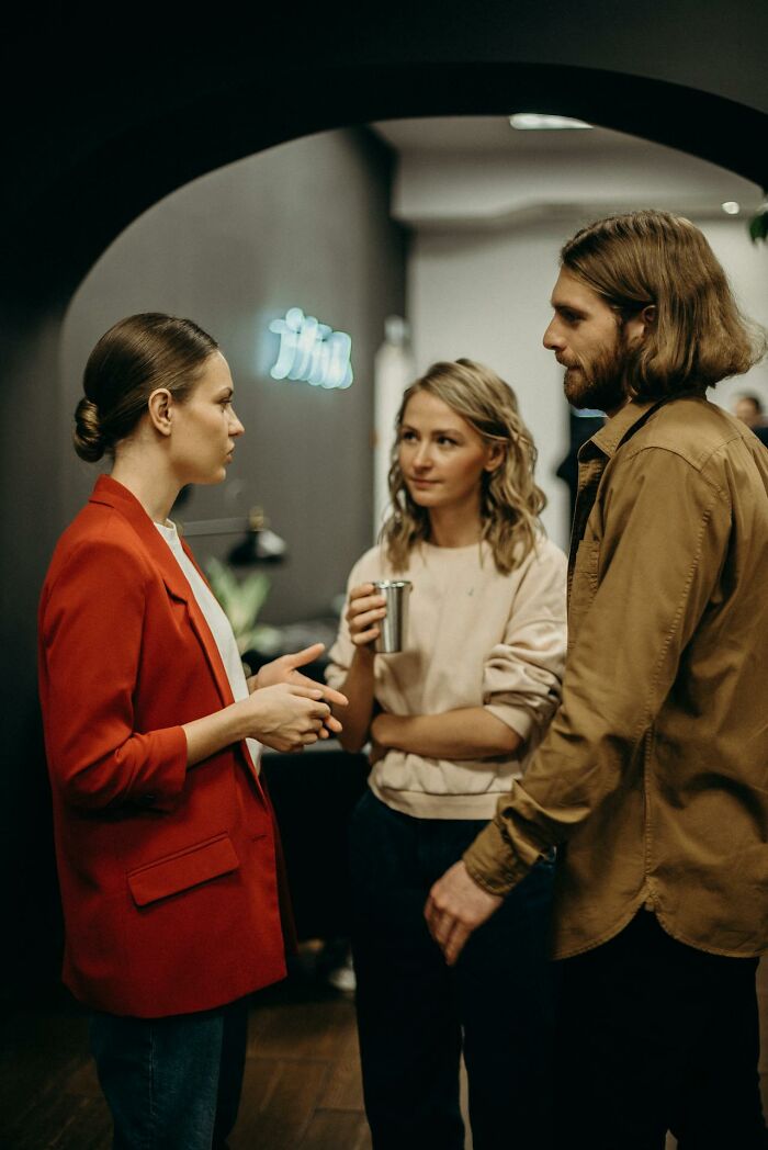 Three people in a tense conversation, woman in red blazer gesturing, scene suggesting creepiest displays of intelligence