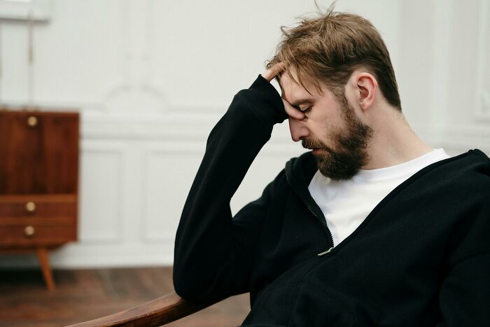 Man with beard sitting indoors looking stressed, reflecting on family secrets in a quiet room with minimalist decor.