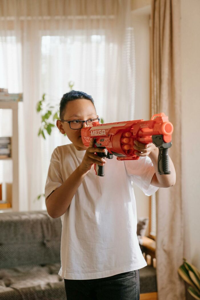 Boy playing indoors with a large orange toy gun, focused during playful 3 AM chaos on the night shift at home.