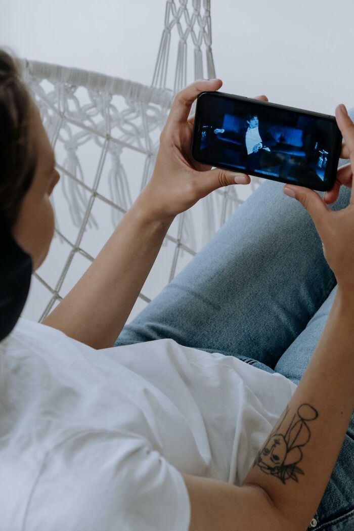 Person with tattoo watching a video on phone while relaxing on a hammock, reflecting on life after prison release.
