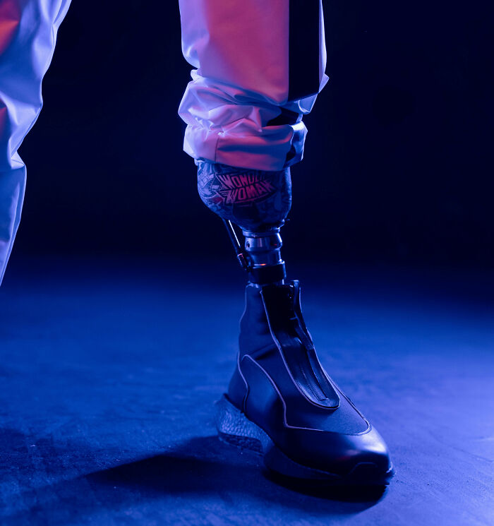 Close-up of a person wearing a futuristic shoe and prosthetic leg in a nightclub with vibrant blue and purple lighting.