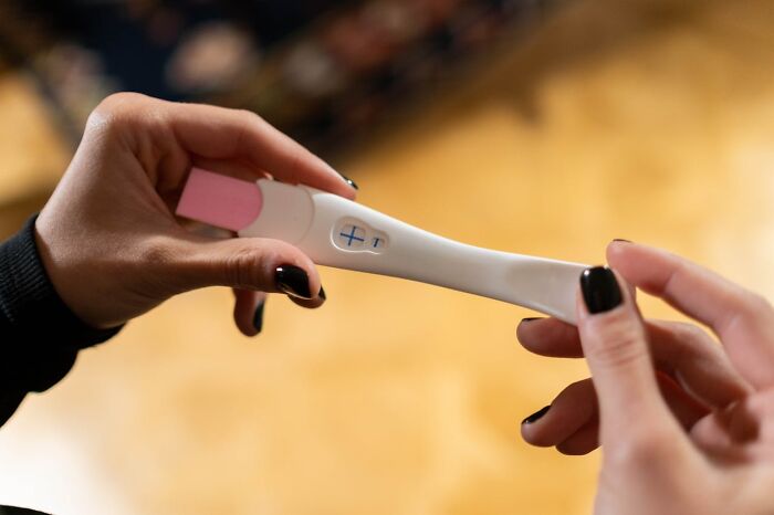 Hands holding positive pregnancy test with plus sign, blurred warm background, rained frogs