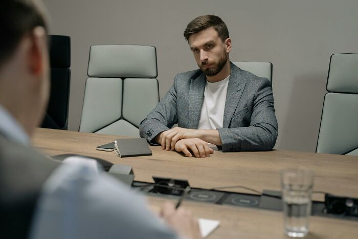 Man in a gray blazer sitting in a conference room during a discussion about bizarre office rules.