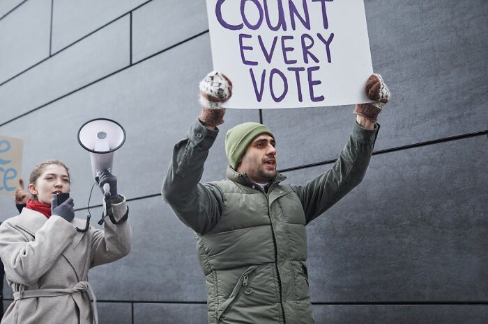 Protester holding count every vote sign outdoors with megaphone supporter highlighting shocks after prison.