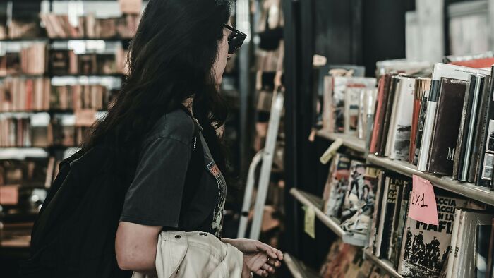 Young woman with long dark hair browsing books on shelves in a store focused on banned books and Harry Potter series. Young woman with long dark hair browsing books on shelves in a store focused on banned books and Harry Potter series.