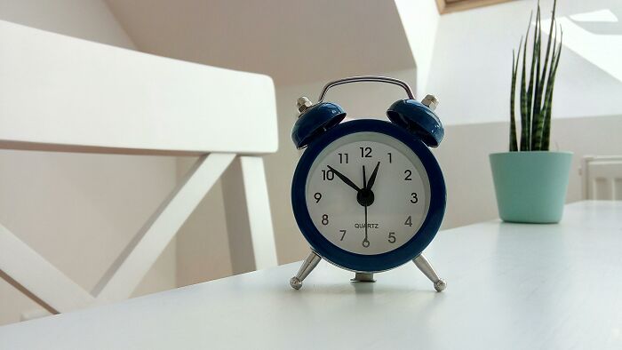 Blue alarm clock on white table near chair and potted plant, illustrating rich people quotes on living with $90K a year.