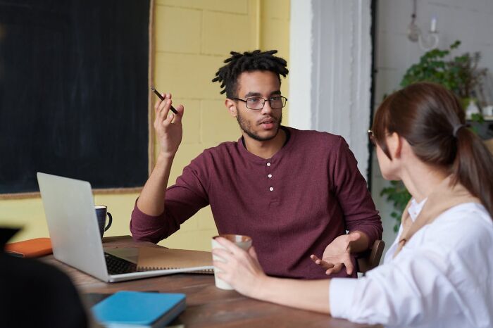 Two colleagues in discussion over a laptop, young man gesturing; scene suggesting creepiest displays of intelligence.