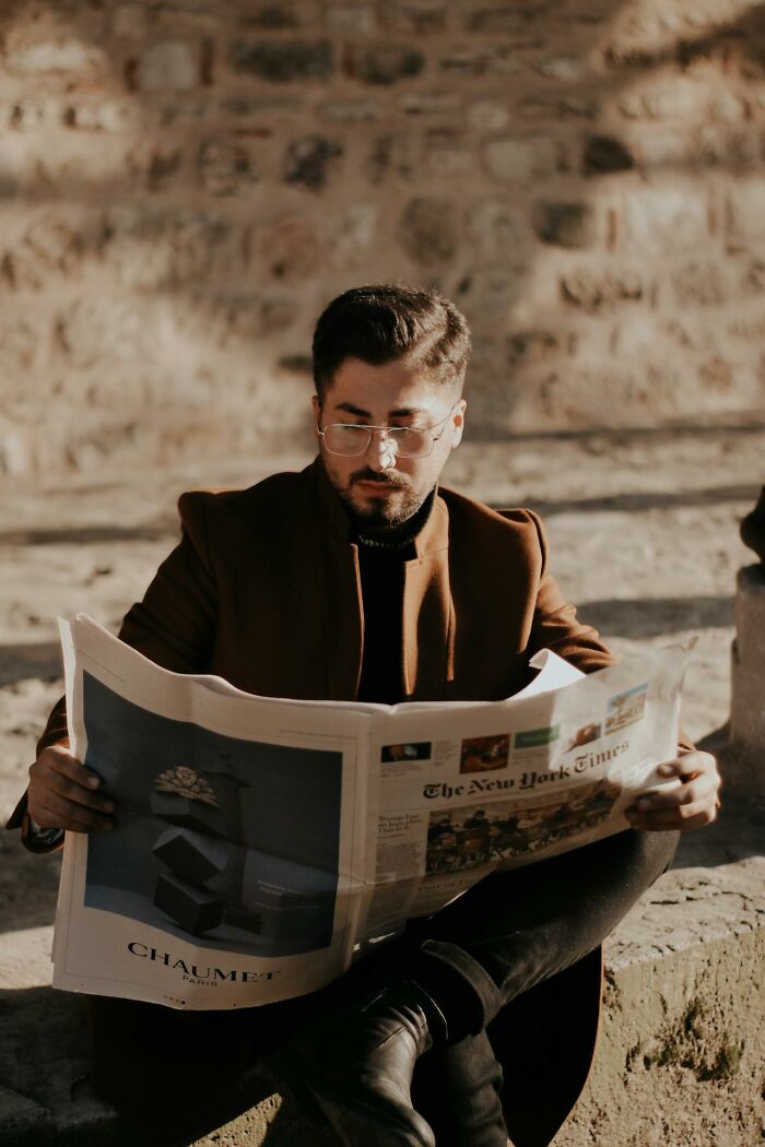 Man wearing glasses and a brown coat reading a newspaper outdoors, reflecting on things that shocked people after prison release.