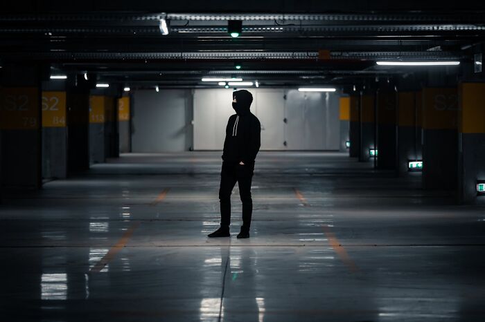 Silhouetted worker standing alone in a dimly lit parking garage during the night shift 3 AM chaos.