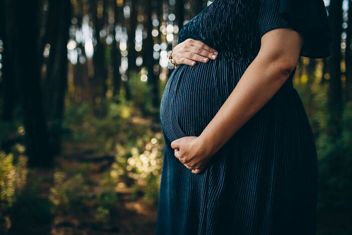Pregnant woman in a dark dress gently holding belly outdoors, symbolizing uplifting stories of progress and hope in America.