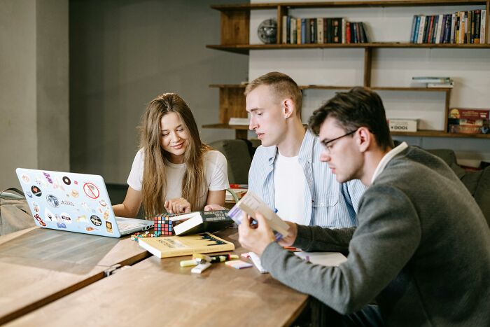 Three young adults taking a 27-question IQ test together, surrounded by books and a laptop in a study room.