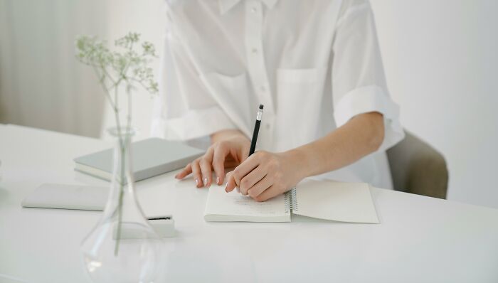 Person writing in a notebook with a pencil, surrounded by books, representing smart words and well-spoken communication. Person writing in a notebook with a pencil, surrounded by books, representing smart words and well-spoken communication.