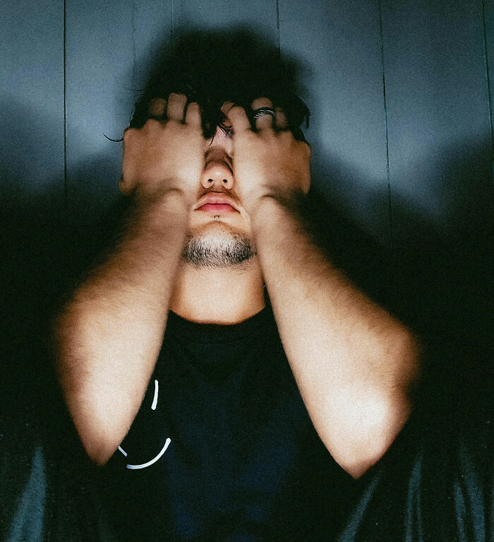 Man covering face with hands in low light illustrating coworkers acting unhinged causing stress and frustration at work.