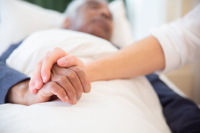 Hospital Workers holding an elderly patient's hand at bedside, comforting final moments.
