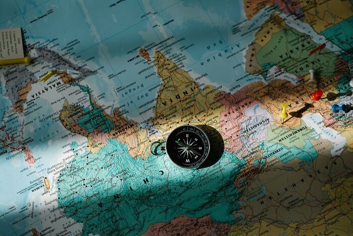 Compass resting on a world map with push pins marking locations, related to geography quiz and map knowledge.