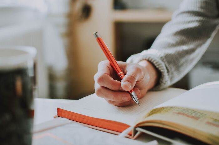 Hand writing in notebook with red pen at desk, journaling about a rained frogs anecdote