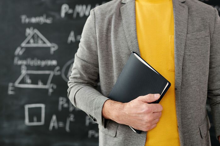 Person in gray blazer and yellow shirt holding a notebook in front of a blackboard with geometric drawings about worst coworkers.