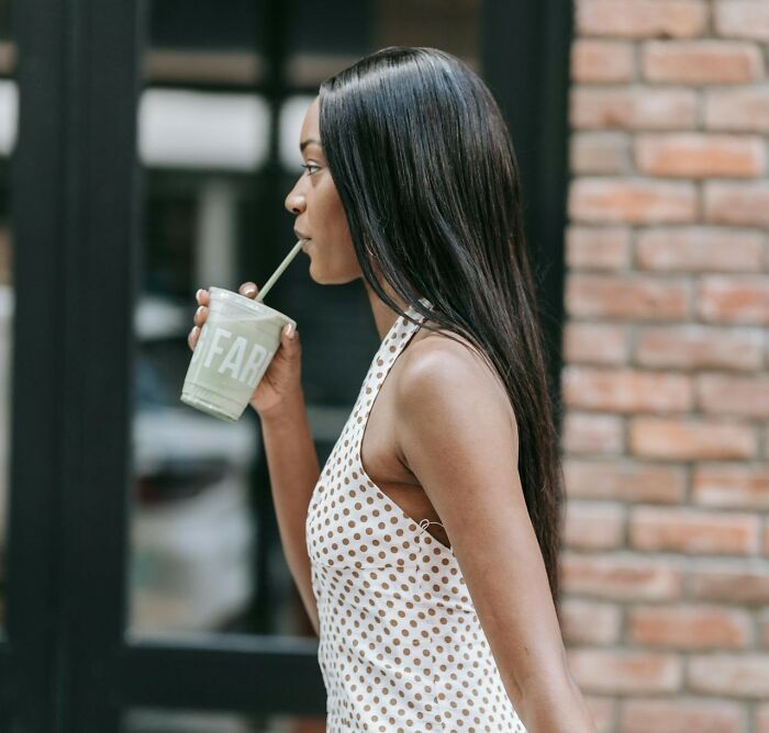Woman with long hair drinking smoothie outdoors, representing things women do to feel safer while living alone. Woman with long hair drinking smoothie outdoors, representing things women do to feel safer while living alone.
