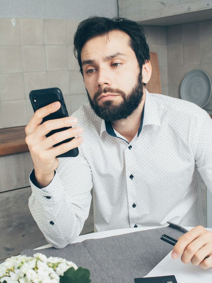 Man with beard looking at his phone with a worried expression, reacting to an accidental text causing panic.